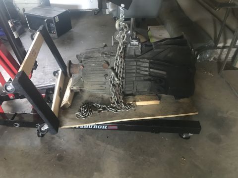 2008 Ford F-250 - Transmission being lifted by a chain hoist, supported by wood blocks and a creeper stand.