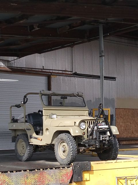 1952 Jeep CJ5 - A tan 1952 Jeep CJ5, equipped with a winch and other front-mounted apparatus, is parked on a loading dock.