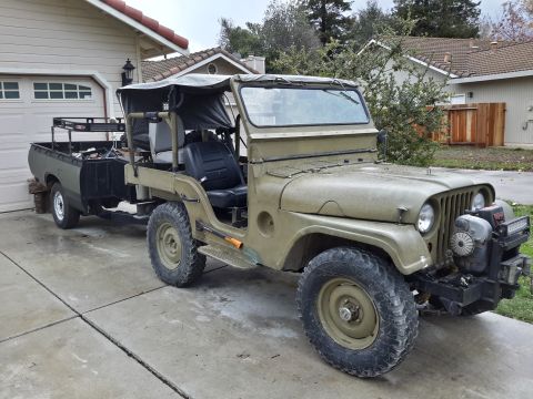 1952 Jeep CJ5 - Olive green 1952 Jeep CJ5 with a trailer attached, parked in a driveway.