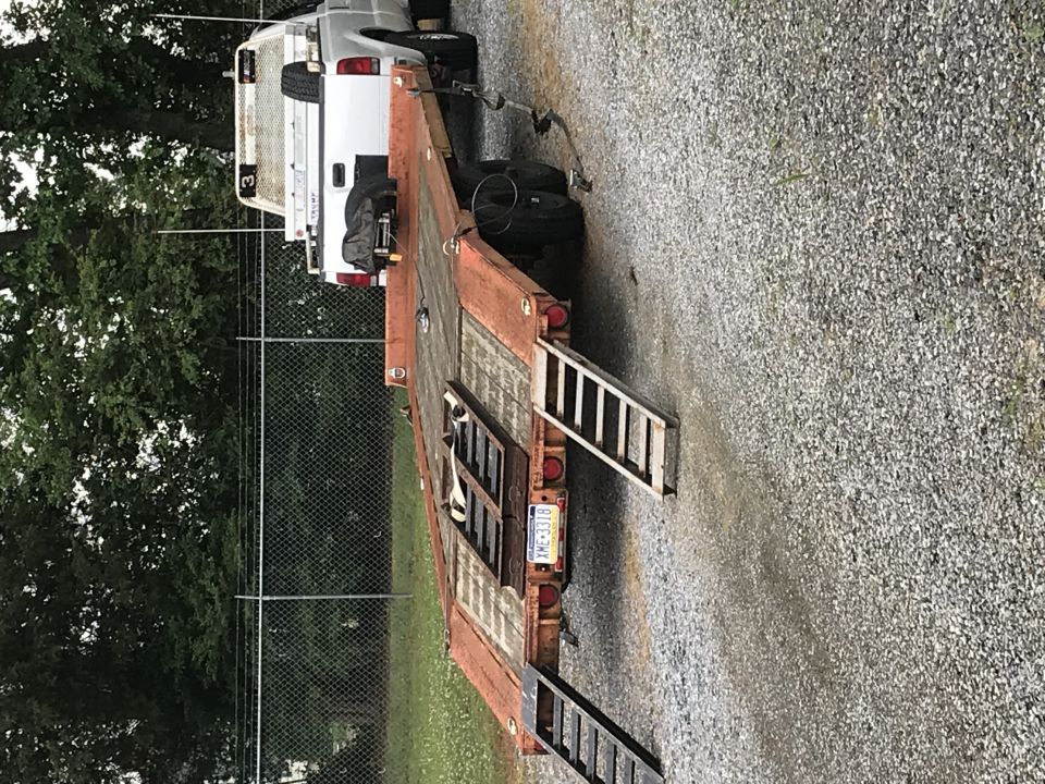 Rusty flatbed trailer behind a white pickup truck with license plate XME-3318.