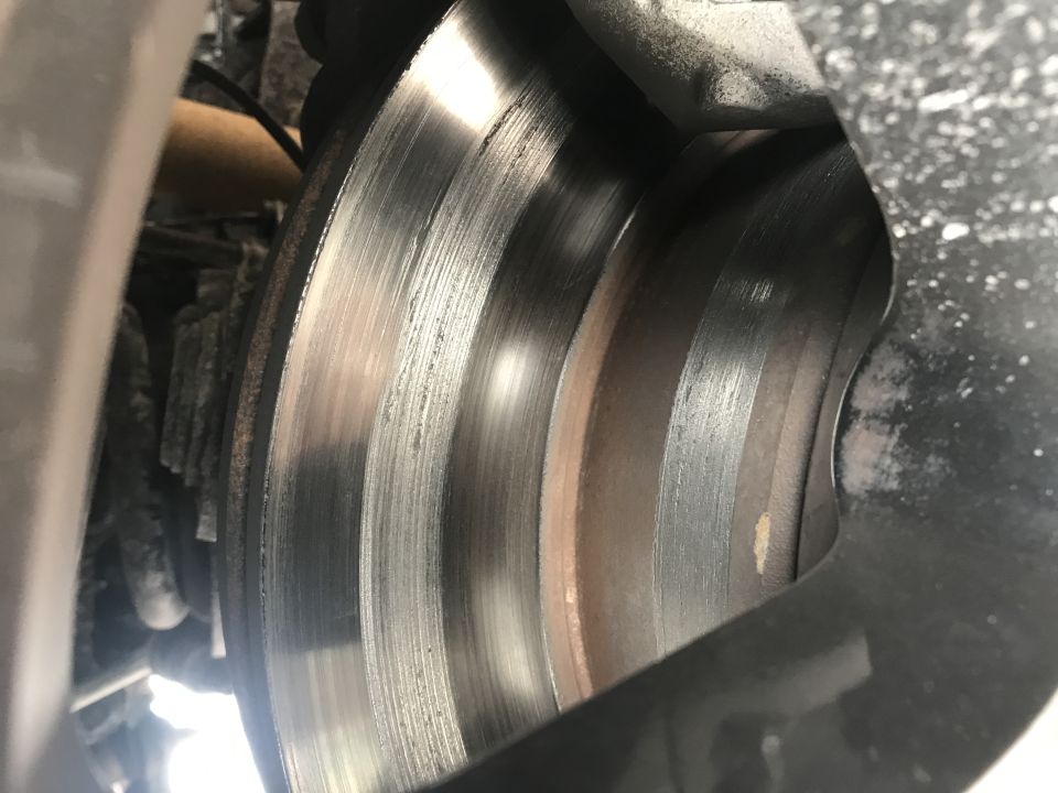 Worn brake rotor with deep grooves and rust, partially visible behind a black brake caliper.