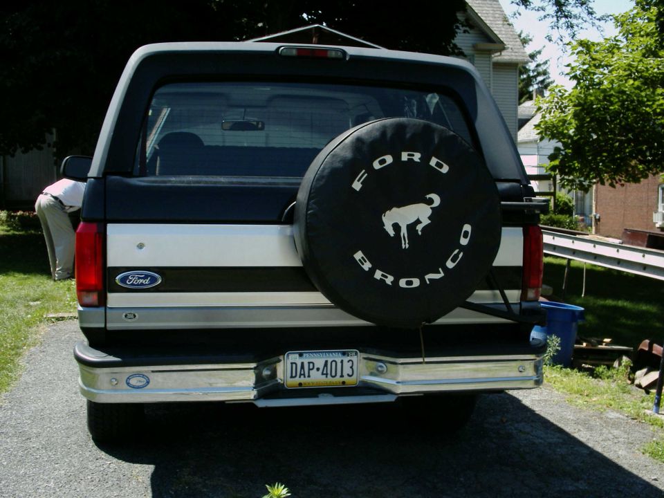 Rear view of a 1990 Ford Bronco with a spare tire cover that says 'Ford Bronco' and shows a horse logo. License plate reads DAP-4013