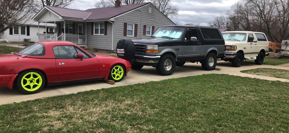 Red Mazda Miata, black and gray Ford Bronco, and white Ford Econoline van parked in a driveway