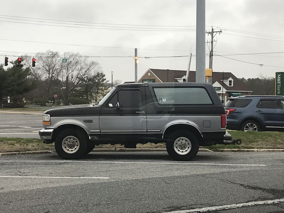1996 Ford Bronco parked on the side of the road, with a blue SUV behind it