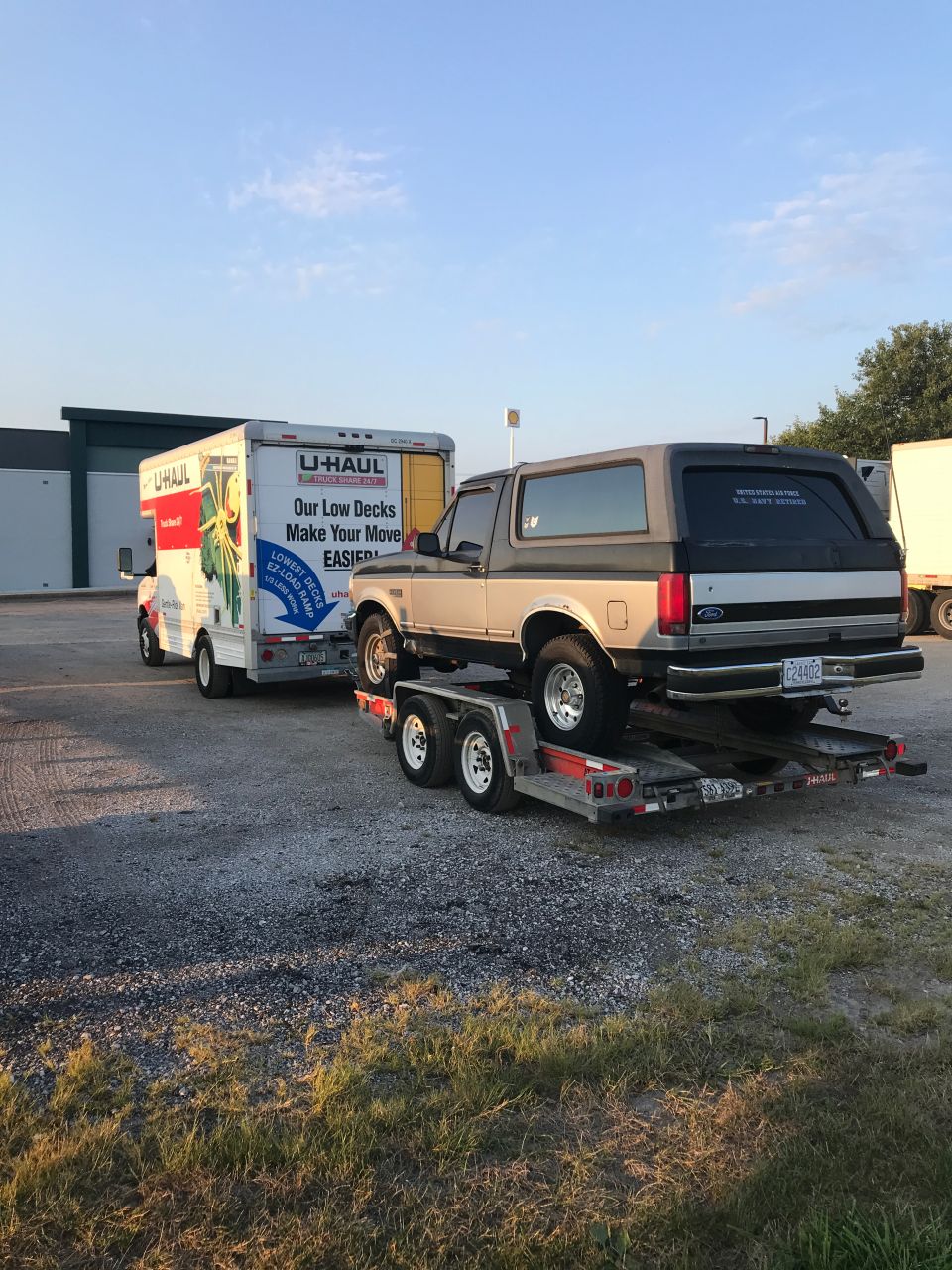 1987 Ford Bronco on a trailer, towed by a U-Haul truck. U-Haul truck has text 'Our Low Decks Make Your Move EASIER'