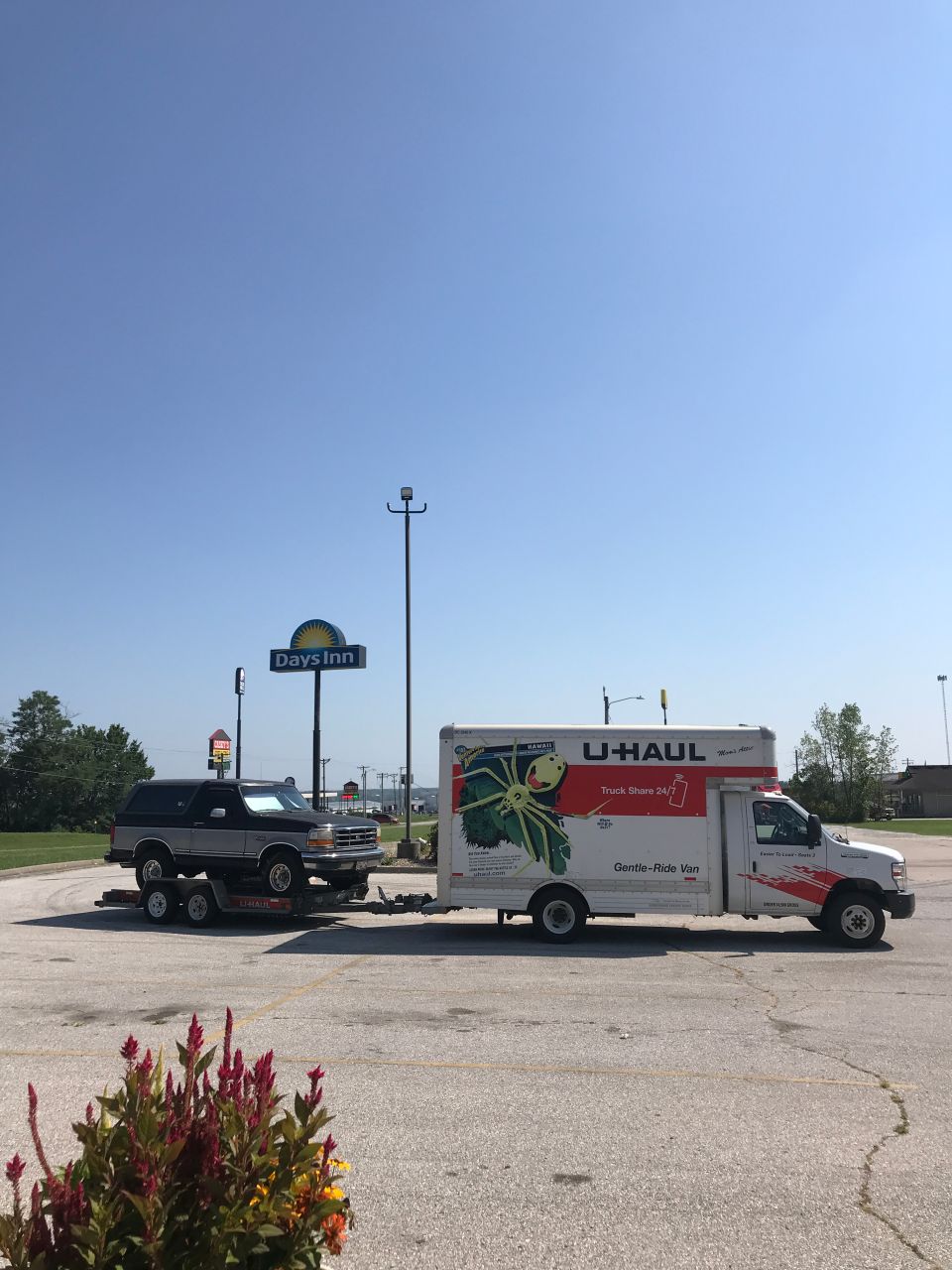 1995 Ford Bronco on a trailer, towed by a U-Haul truck, parked at a Days Inn