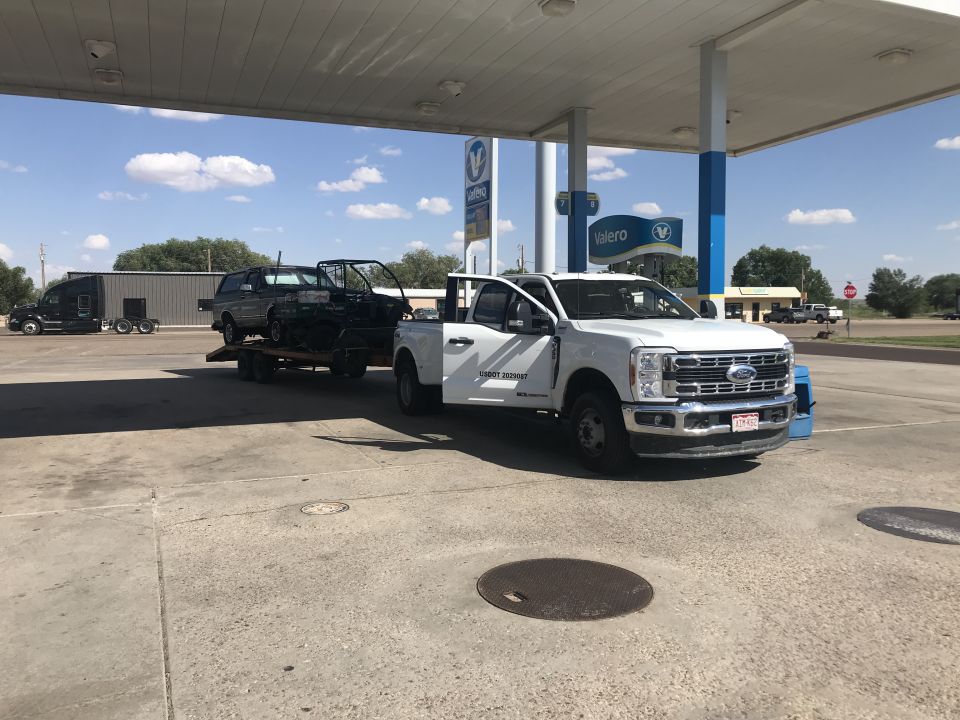 White Ford F-350 Super Duty truck towing a trailer with a car body, parked at a Valero gas station