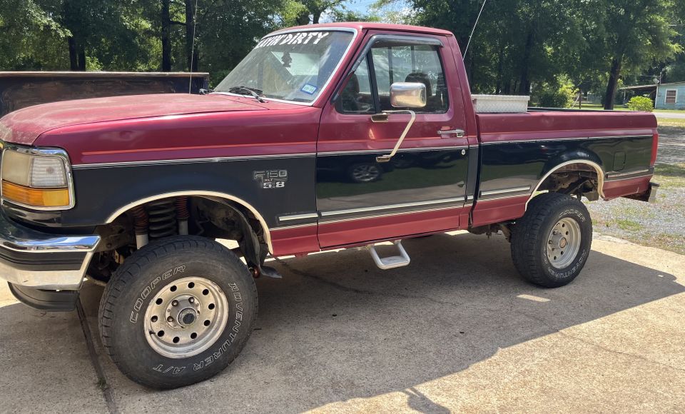 Red and black Ford F-150 pickup truck with lifted suspension and off-road tires.