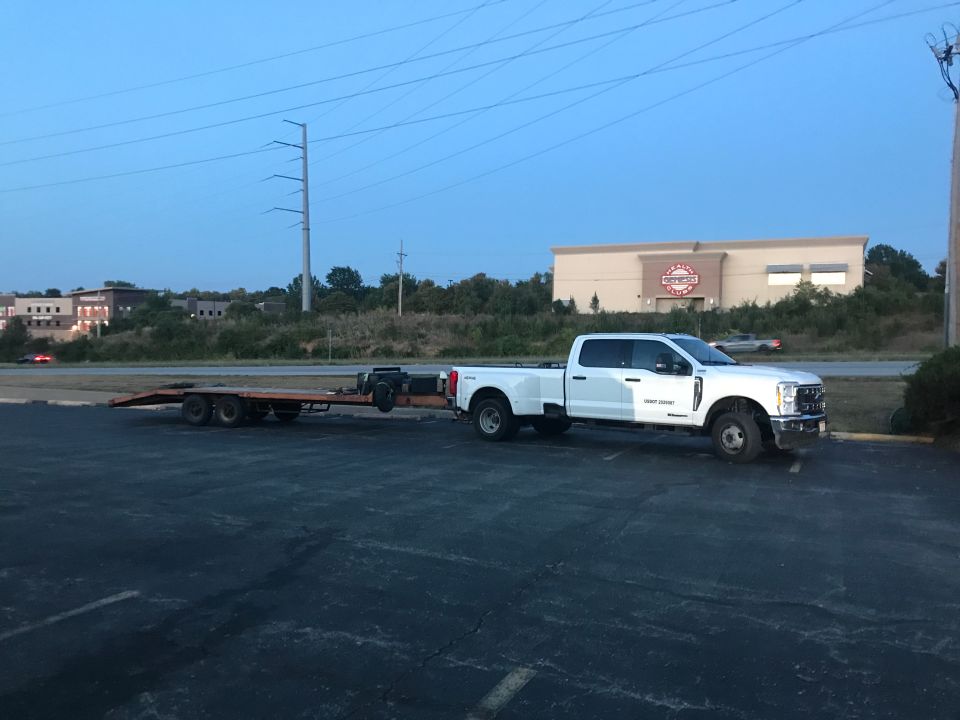 White Ford F-series Super Duty dually pickup truck towing an orange flatbed trailer.