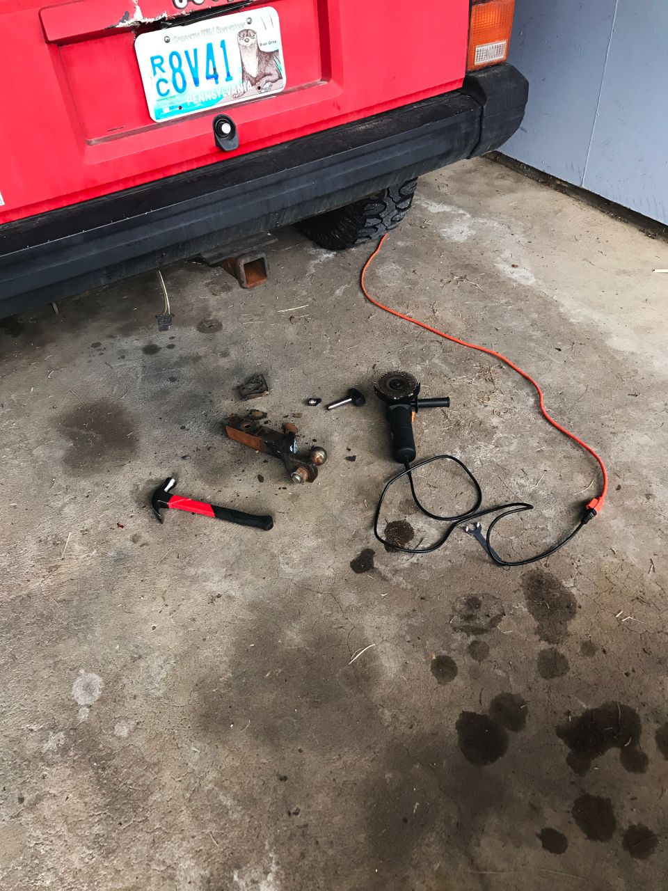 Red Jeep Cherokee rear with license plate R8V41, hammer, and angle grinder on concrete floor.