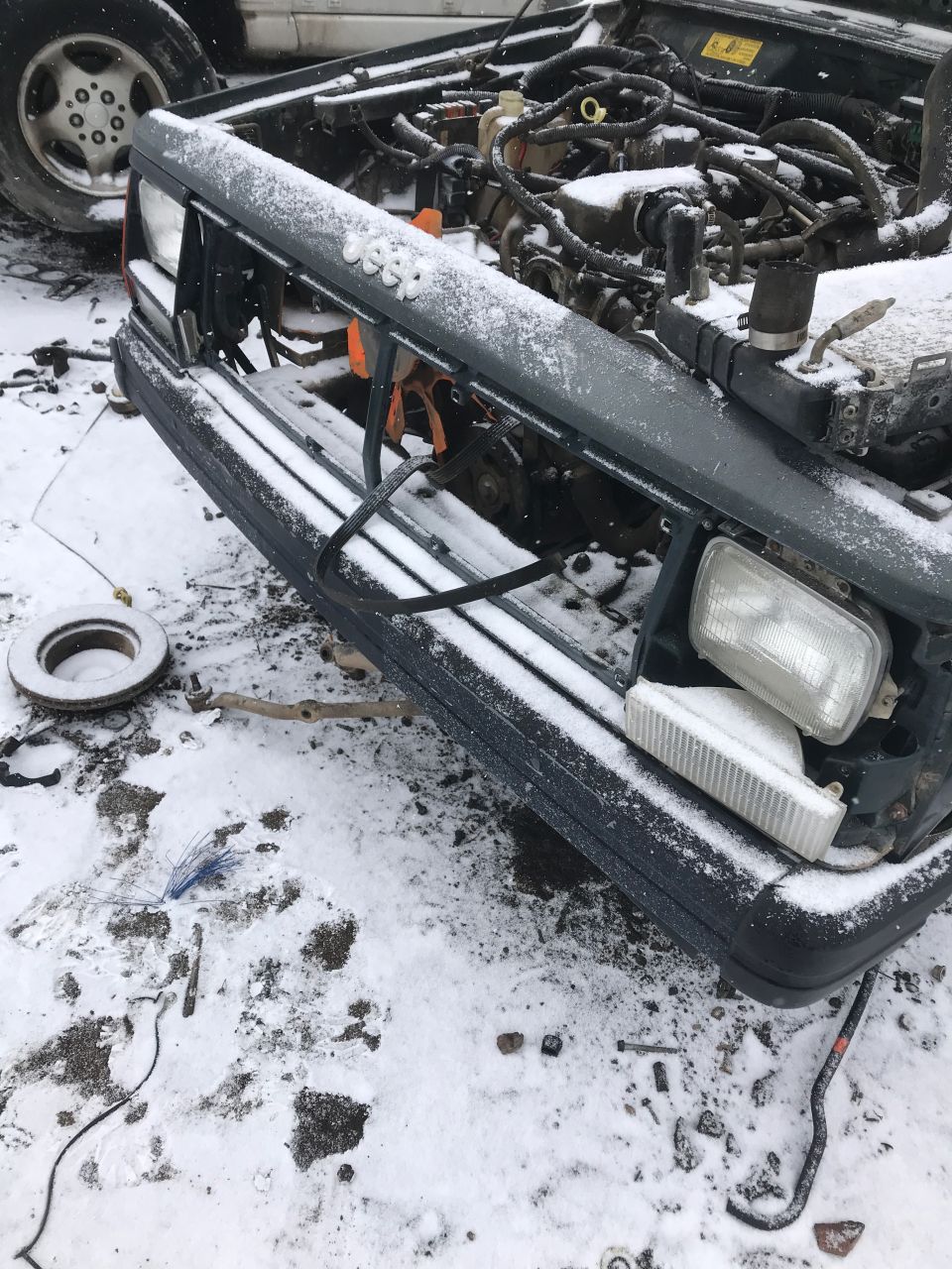 Snow-covered front of a dark gray Jeep Cherokee with open hood and engine visible.