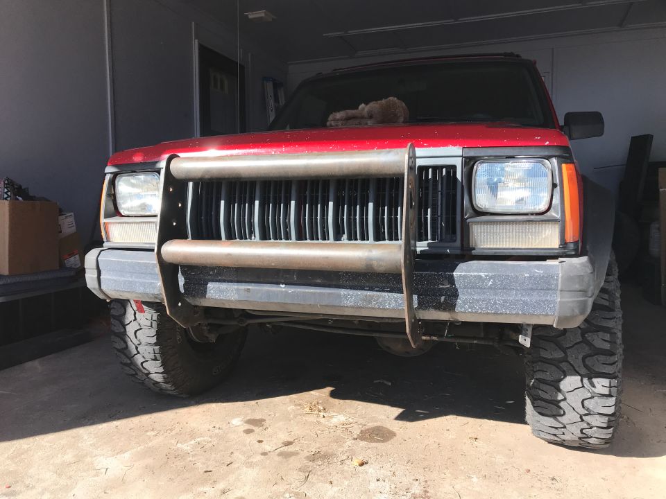 Red Jeep Cherokee with brush guard and off-road tires, parked indoors.