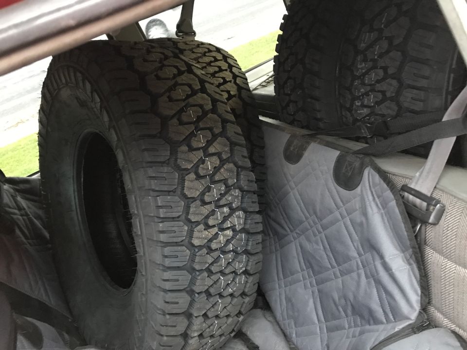 Two off-road tires in a vehicle cargo area on a gray mat.