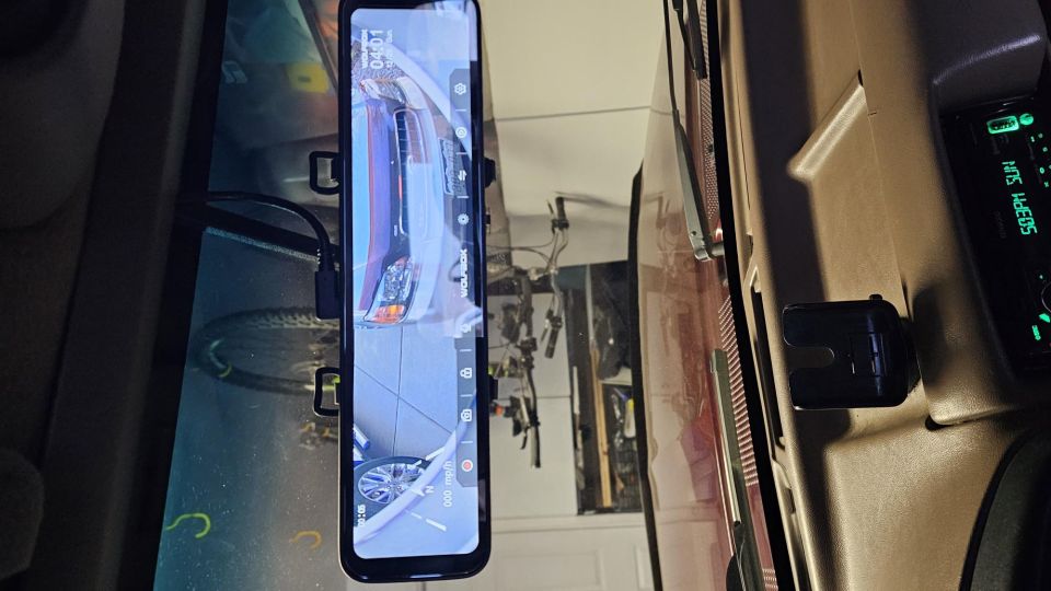 Rearview mirror dashcam showing car front, time 04:01, and vehicle interior with dashboard stereo.