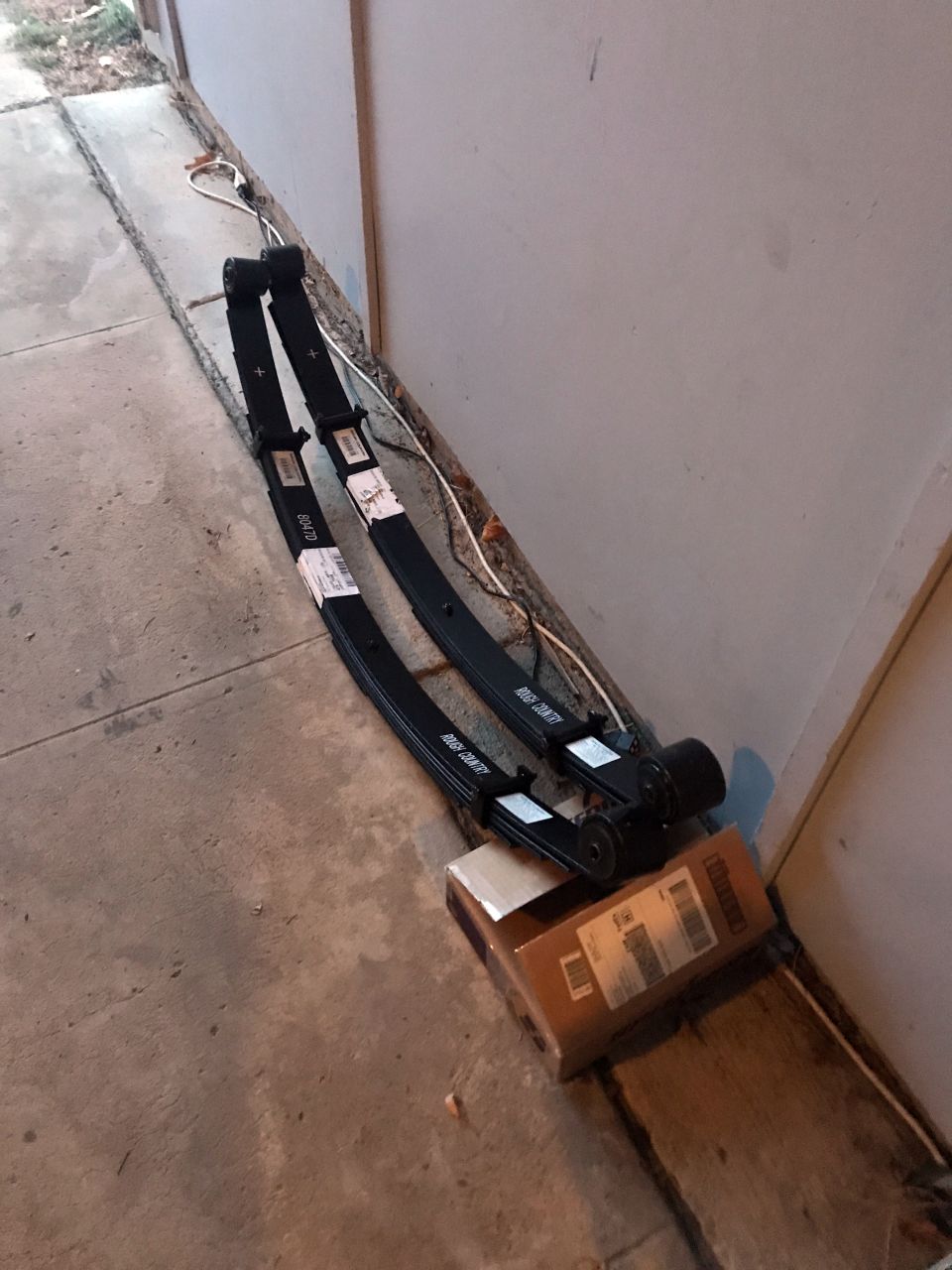 Two black Rough Country leaf springs with white labels on a concrete surface.