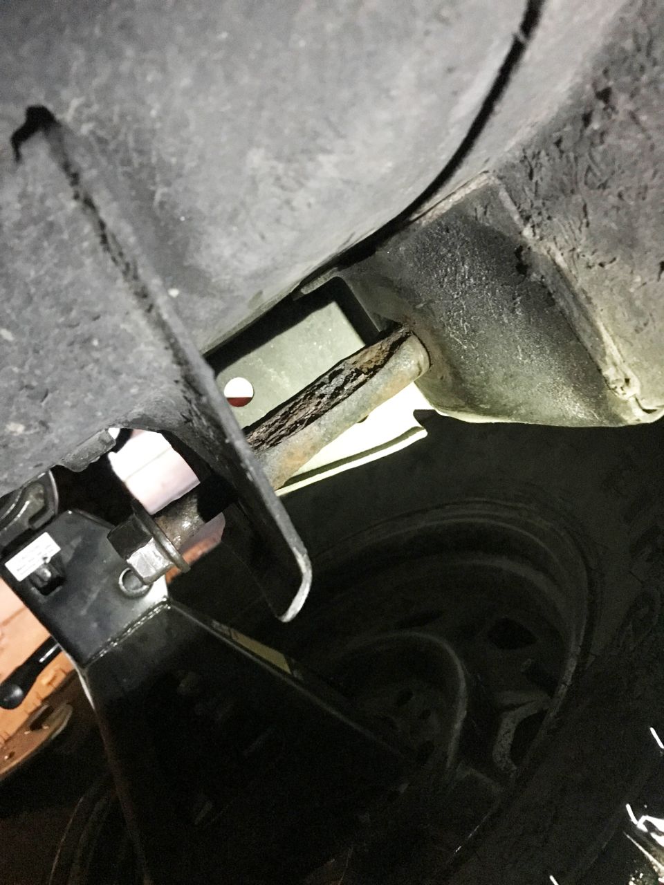 Close-up of rusty metal bar on vehicle undercarriage supported by a black jack.