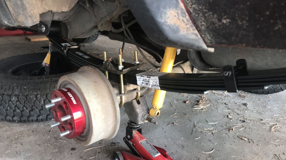 Jeep Cherokee rear suspension with new leaf springs, yellow shocks, red wheel spacer, jack and stand.