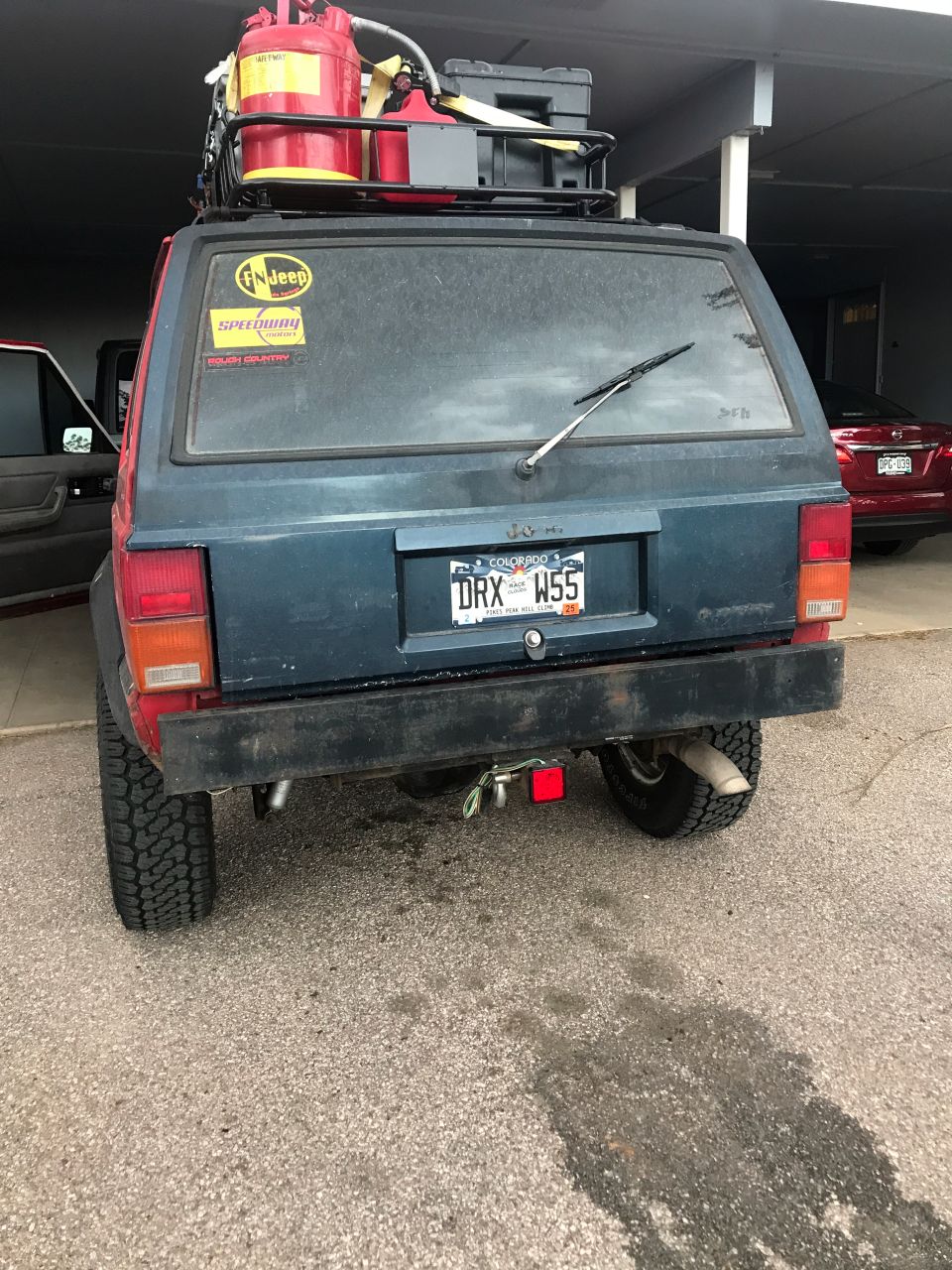 Rear view of a dark blue Jeep Cherokee with roof rack, jerry cans, and Colorado license plate.