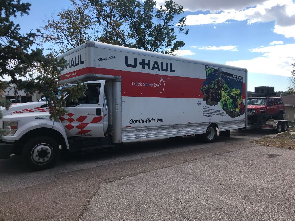 White U-Haul truck parked next to a red Jeep Cherokee towing a trailer.