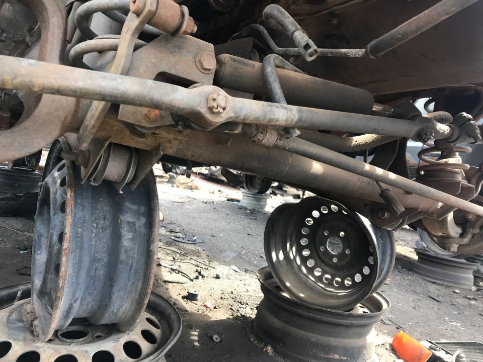 Close-up of rusty vehicle suspension, steering linkage, and two damaged wheels.