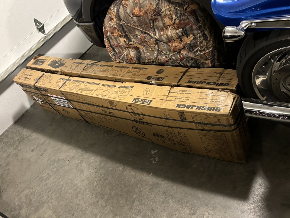 Two stacked cardboard boxes labeled QUICKJACK next to a motorcycle.