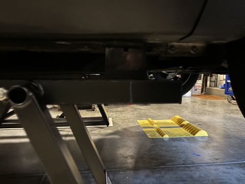 1974 Dodge Challenger - The underside of a vehicle is visible, supported by a lift. Wheel chocks are placed on the garage floor.