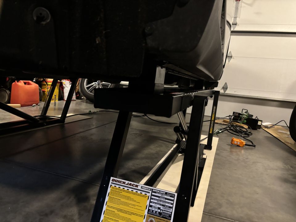 Car chassis elevated on a QuickJack lift with orange gas can in background