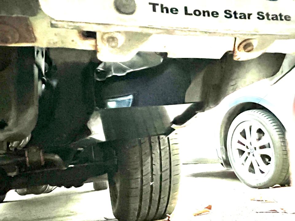 Underside view of a vehicle on a lift with Texas Lone Star State plate and alloy wheel