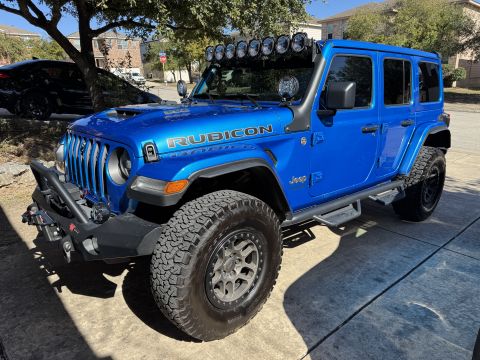 2022 Jeep Wrangler - A bright blue Jeep Wrangler Rubicon is parked on a driveway, equipped with a light bar and off-road tires.