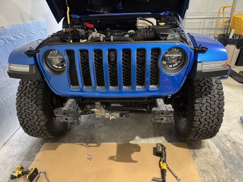 2022 Jeep Wrangler - A blue Jeep Wrangler is shown with its hood open and front bumper removed, revealing the engine and chassis.