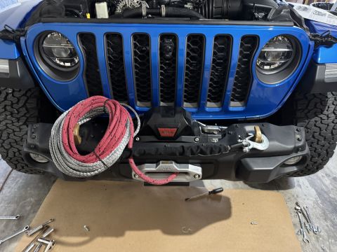 2022 Jeep Wrangler - A blue Jeep Wrangler's front bumper and grille are shown with a WARN winch and coiled rope, suggesting an upgrade or modification.