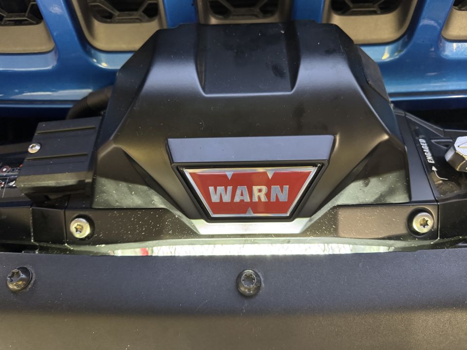 Warn winch mounted on a blue vehicle's front bumper, with Supermotors.net logo at bottom right