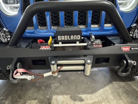 2022 Jeep Wrangler - The front of a blue Jeep Wrangler is shown, a winch and tow strap. The vehicle is equipped with aftermarket bumper accessories.