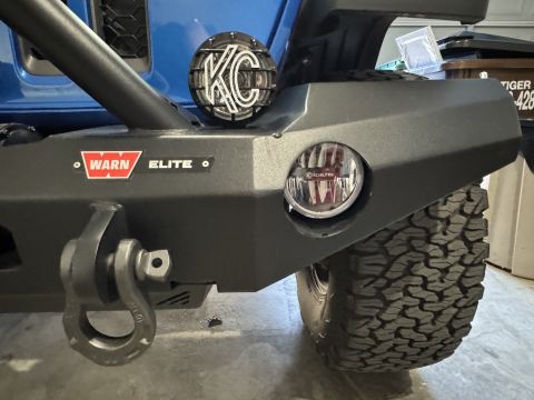 2022 Jeep Wrangler - Close-up of a blue Jeep Wrangler's aftermarket front bumper, equipped with KC lights and a Warn Elite winch mount.