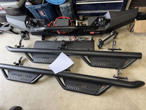 2022 Jeep Wrangler - Aftermarket off-road bumper and side steps laid out on a garage floor.