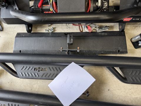 2022 Jeep Wrangler - Parts laid out on the ground, including a winch, skid plate, and side steps, with a handwritten note.
