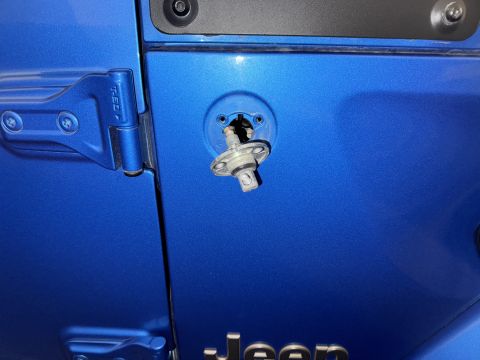 2022 Jeep Wrangler - Close-up of a blue Jeep door showing the removed antenna mount and part of the Jeep logo.