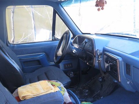 1988 Ford Bronco - The interior of a blue pickup truck, likely from the 1980s, shows worn cloth seats and a functional dashboard.