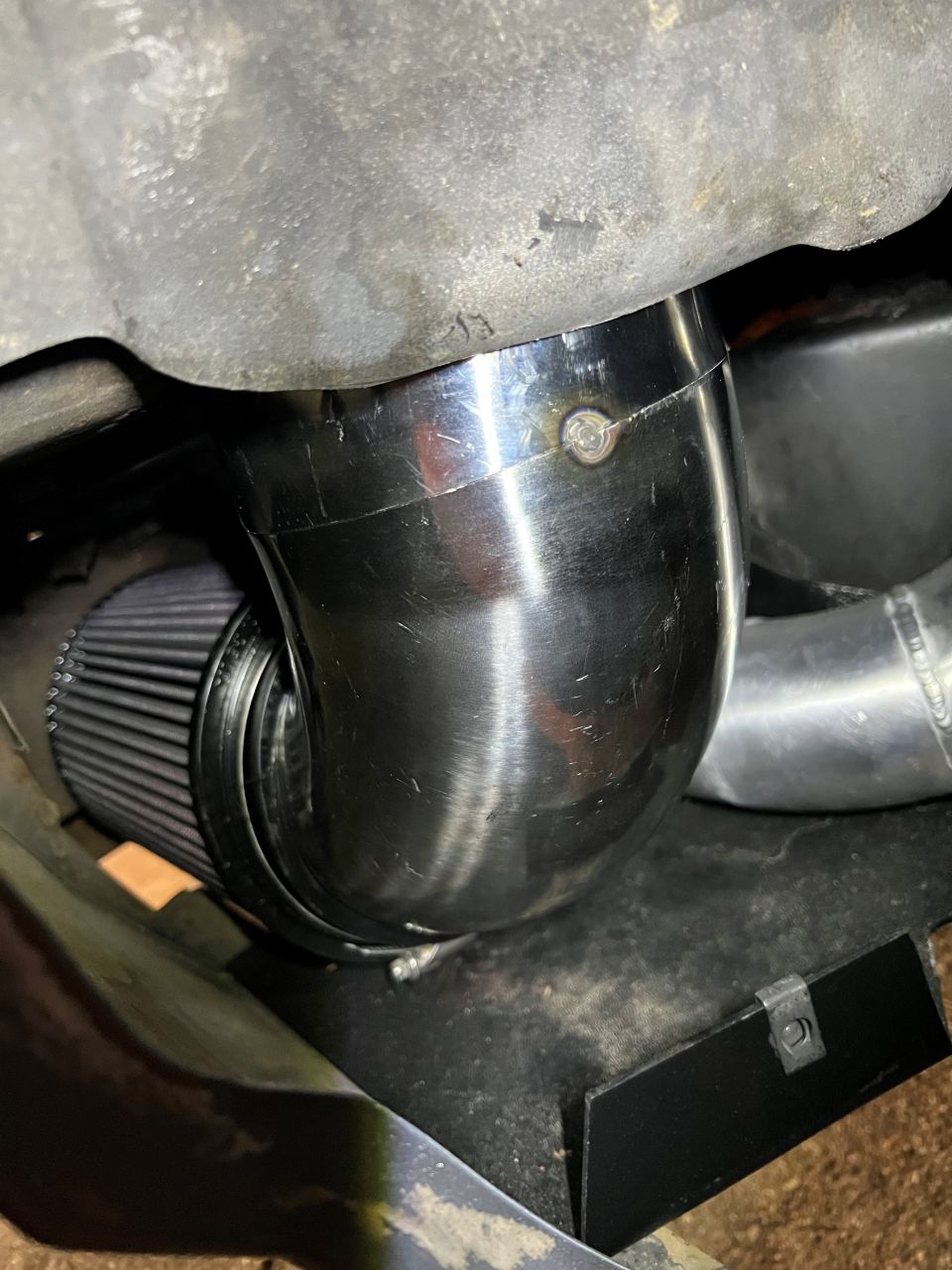 Chrome turbo intake pipe connected to a black air filter, mounted under a gray metal surface
