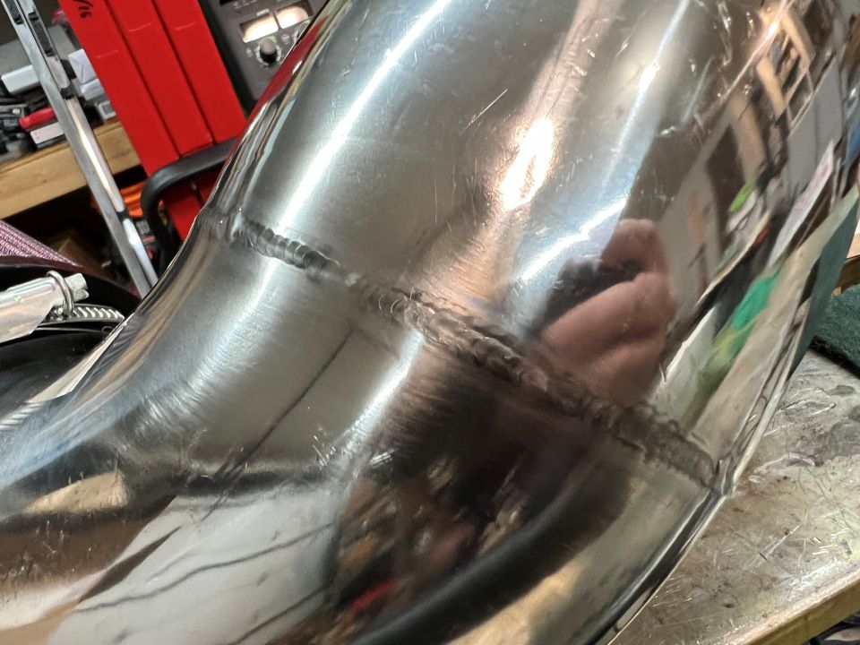 Polished metal exhaust pipe with weld seams in a workshop setting.