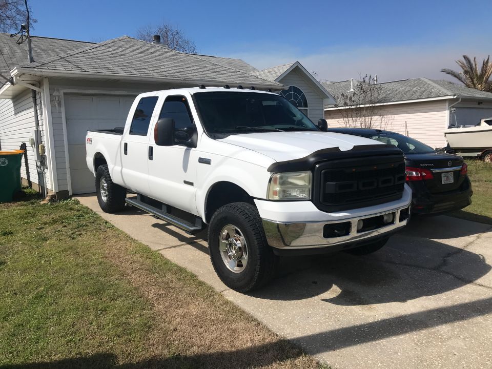 White Ford F-250 Super Duty pickup truck parked in driveway with black Nissan Sentra and boat in background.