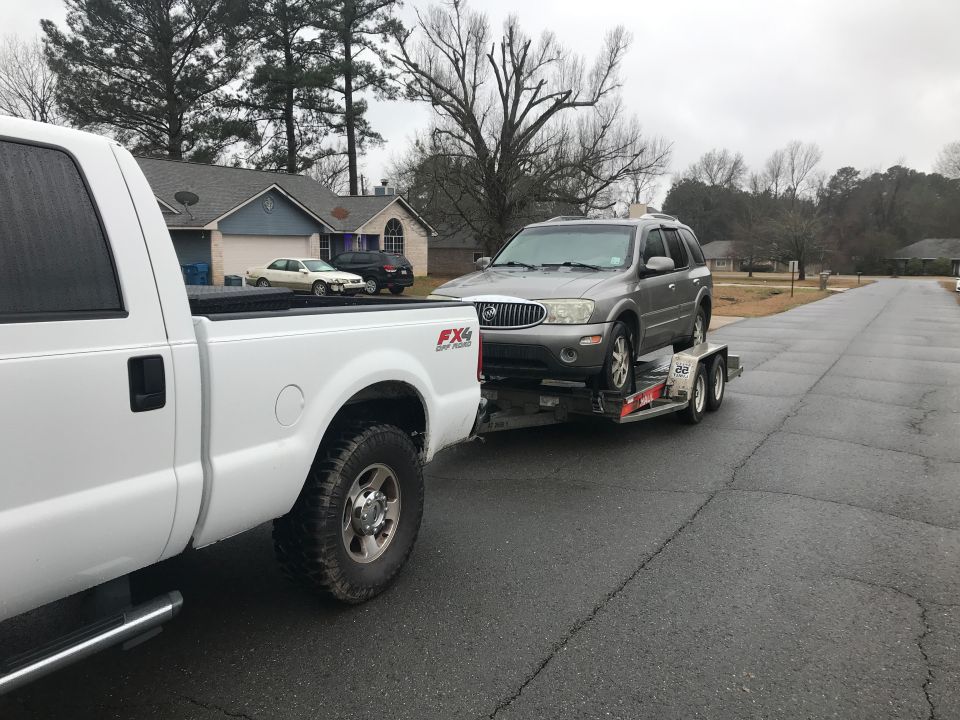 White Ford F-250 pickup truck towing a silver Buick SUV on a trailer.