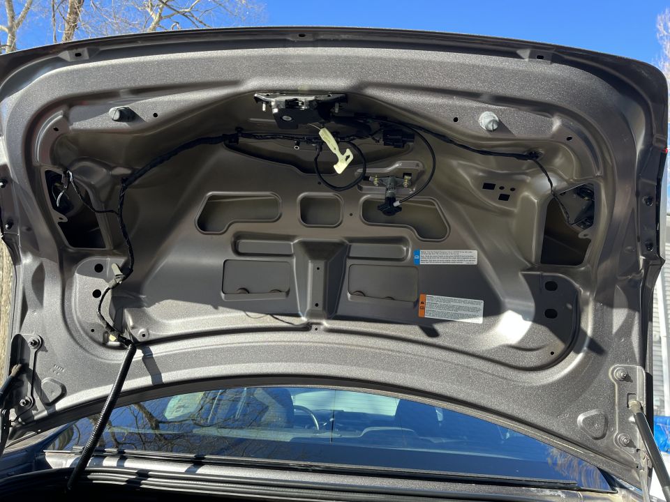 Underside of an open trunk lid showing latch, wiring and stamped sheet metal