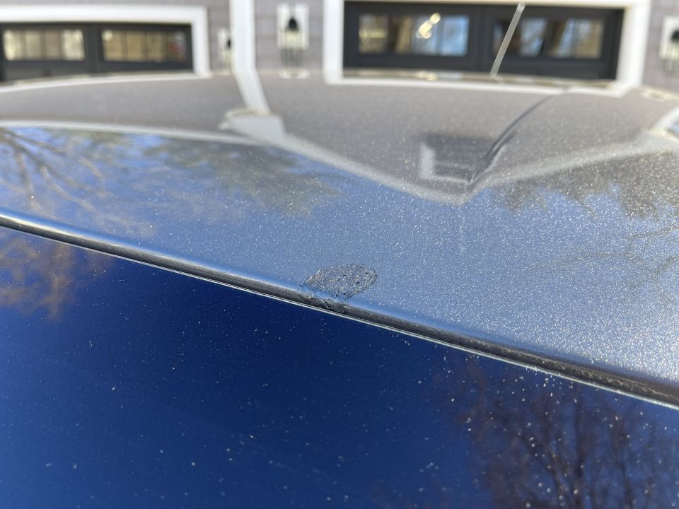 Close-up of a dark blue car roof and pillar with paint reflections