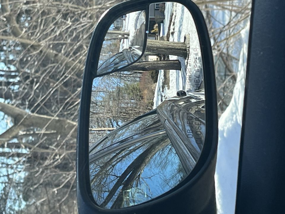 Driver side mirror reflecting trees and a snowy yard