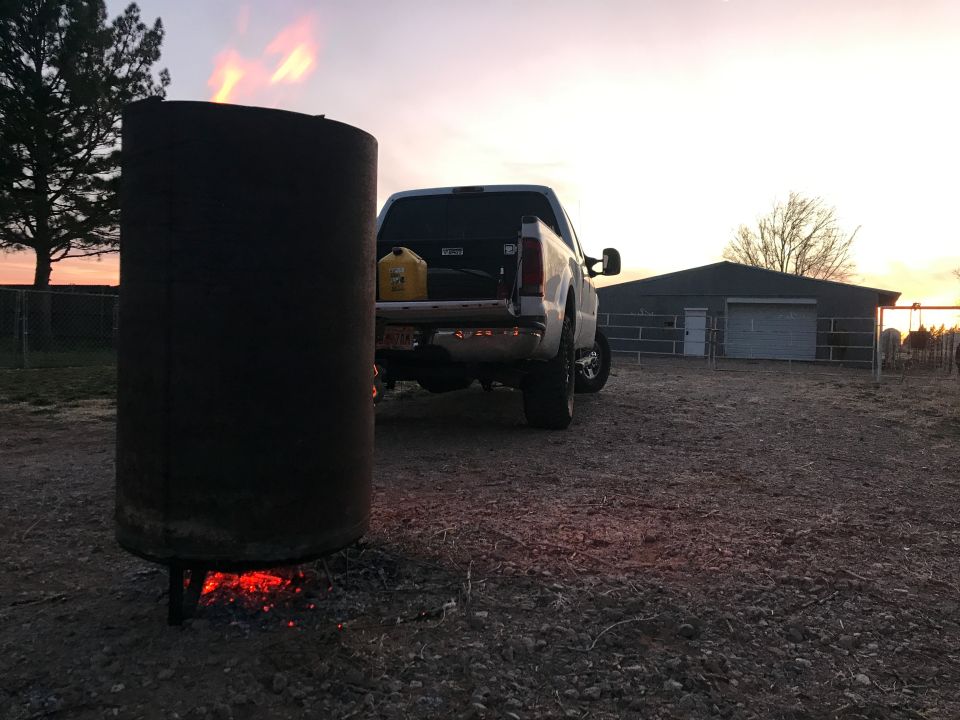 White Ford F-250 pickup truck parked next to a burning barrel at sunset.