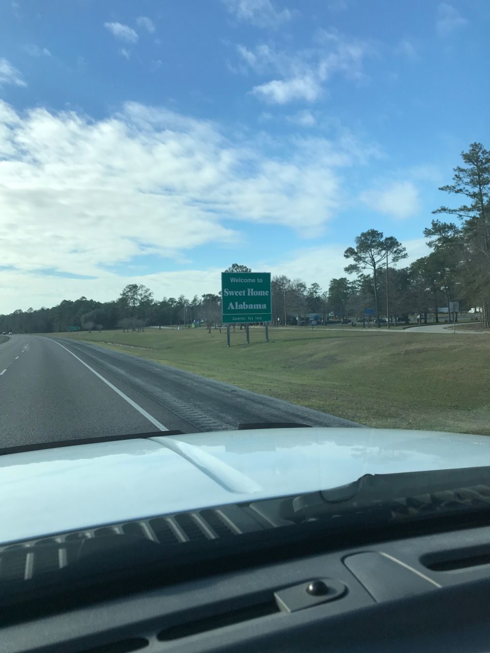 Welcome to Sweet Home Alabama sign on a highway, viewed from inside a vehicle.