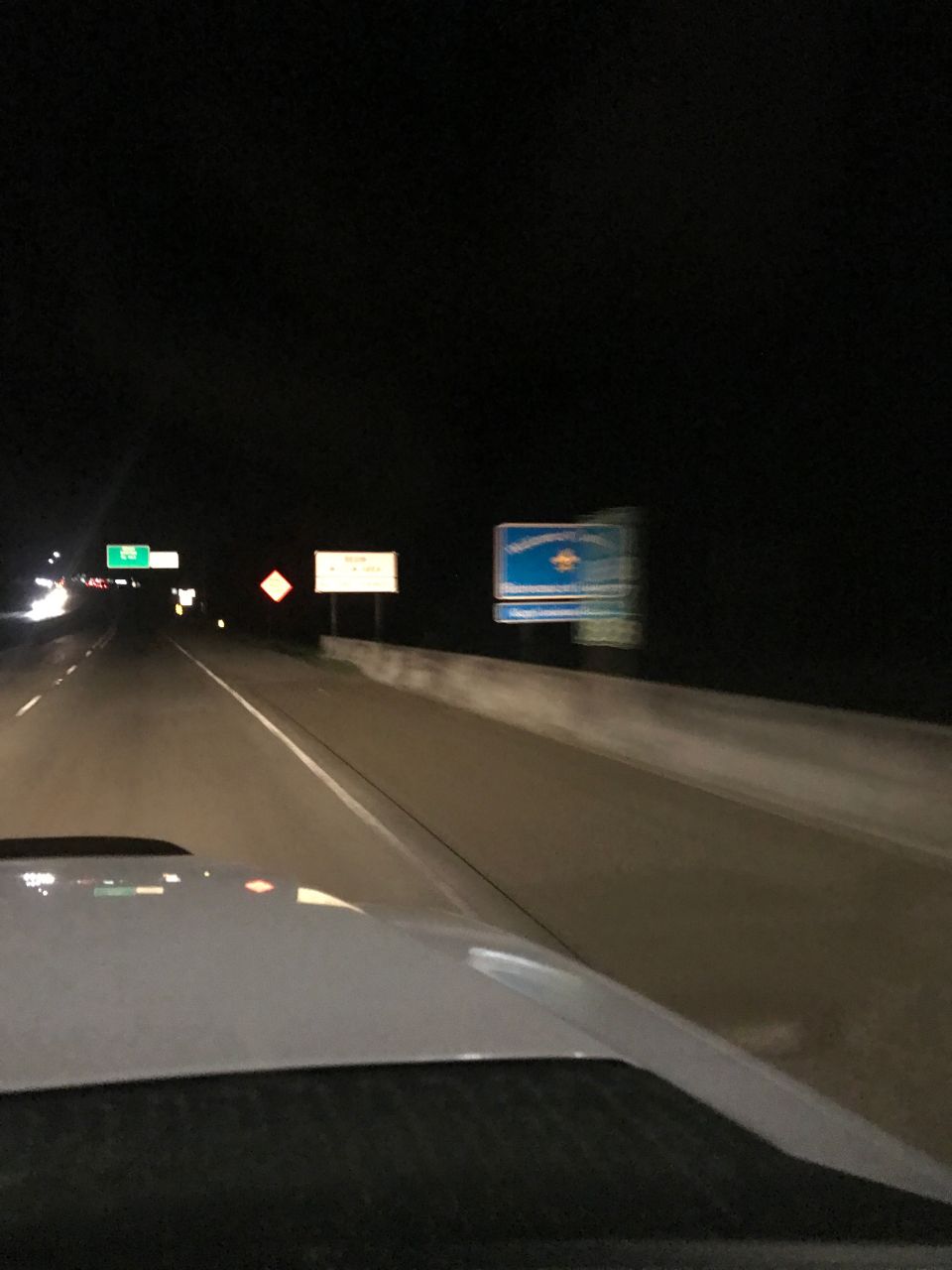 Nighttime highway view through a windshield with road signs and a billboard