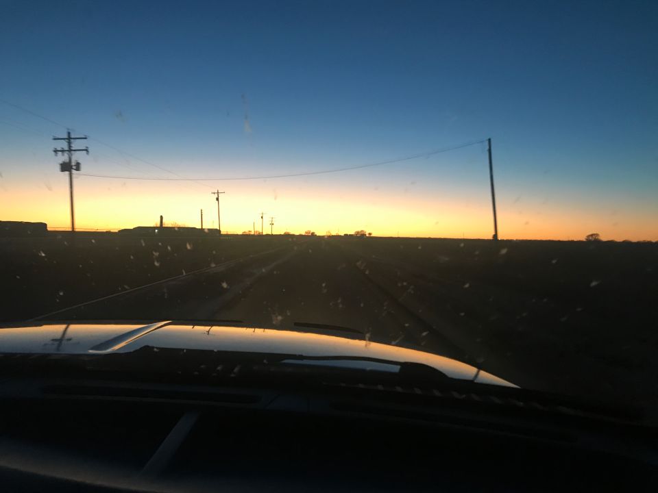 View through windshield of rural road at sunset with power lines