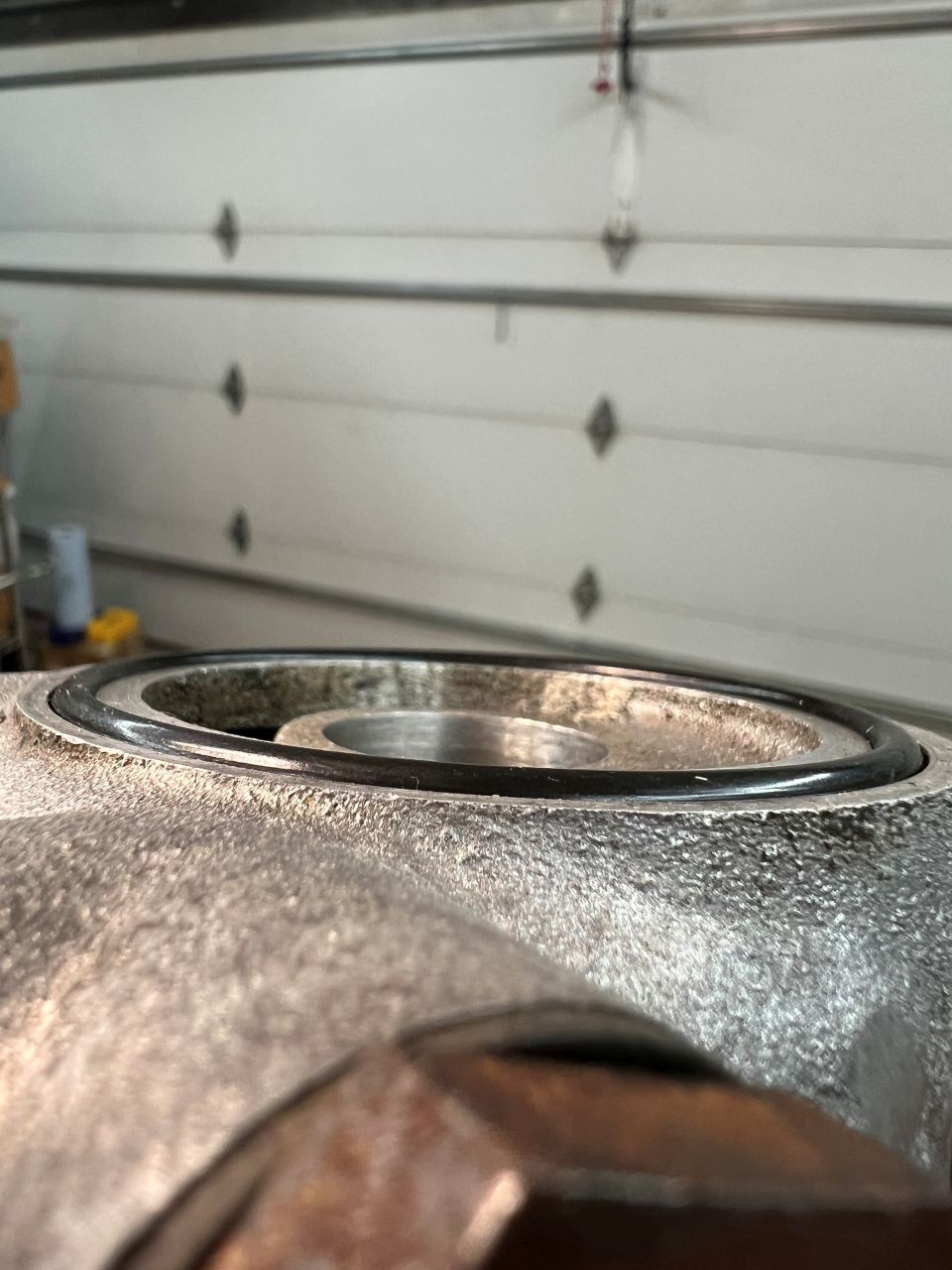 Close-up of a black O-ring seal in a metal housing with a garage door in the background.